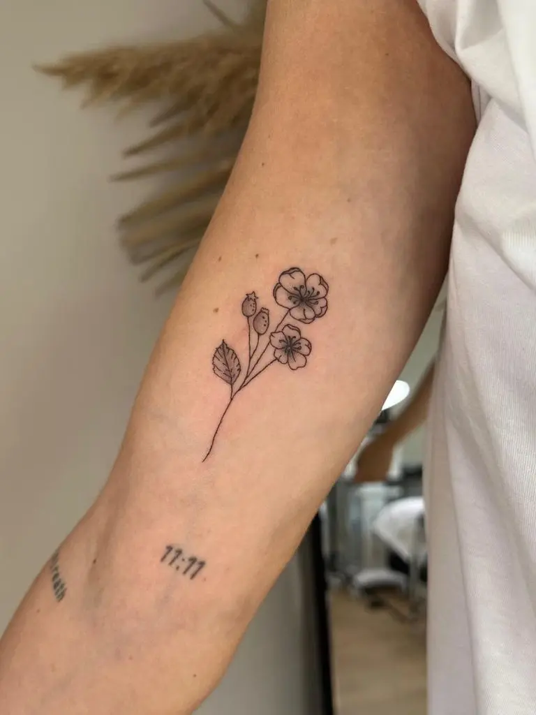 Fine line flower tattoo on a woman's arm by Sophie