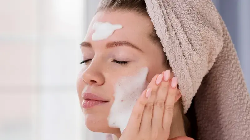 A woman washing her face with retinols, acids, and exfoliants which can cause premature fading if applied over brows.